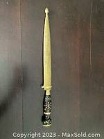 Full view of the sword with golden embossed blade and ornate handle upright on dark background
