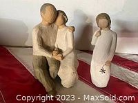 Two figurine statues, man and woman embracing and woman holding flower, displayed on red and white surface.
