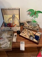 Multiple jewelry display trays and boxes filled with rings, pins, necklaces, earrings, and an earring holder stand on a wood table.