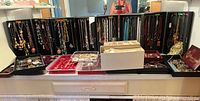 Wide view of multiple black folding display panels with hanging necklaces and various storage trays in front filled with bracelets, earrings and pins.