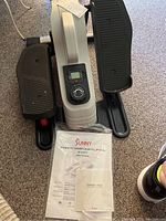 Top view of elliptical pedals, resistance knob, and digital screen, with user manual and thank you card placed in front.