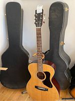 Front view of Madeira acoustic guitar with two hard-shell cases behind on hardwood floor