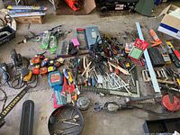 Wide photo showing a large assortment of hand tools laid on the floor including wrenches, pliers, tape measures, electric sander, hand saws, and hammers explaining the lot size and variety