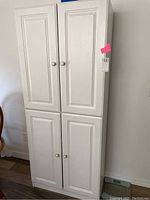 Tall white/off-white veneered MDF kitchen cabinet with four paneled doors, standing upright against a wall.
