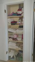 Full view of linen closet with multiple shelves containing assorted towels, linens, and trash bags.