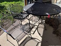 Photo showing two of the four metal mesh chairs and the round metal mesh patio table with an umbrella hole in the center on a concrete patio.
