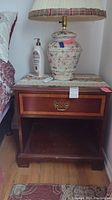 Wooden Kimball nightstand with a single drawer and open lower shelf. Brass handle is visible on drawer front. An ornate lamp and lotion bottle rest on top for scale.