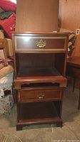 Pair of wooden nightstands stacked, showing drawer with brass handles, decorative gold trim, and lower open space.