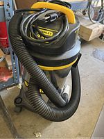 Full view of Stanley wet/dry shop vac showing black and yellow top, metal body, coiled hose and power cord.