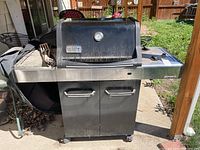 Full view of the Weber Spirit gas grill showing the main grill body, side burner, handles, wheels, and part of the cover and tools on the side.