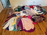 Wide view of over 50 pieces of women's clothing laid out on the floor showing mix of tops, scarves, and bottoms in various colors and patterns.
