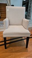 Front view of upholstered beige armchair showing seat, backrest, and armrests with slight wear visible.