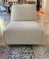 Front view of beige upholstered chair showing seat and backrest in neutral fabric with subtle texture on tiled floor.