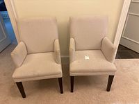 Two cream color armchairs side by side against a wall, showing front and side angles.