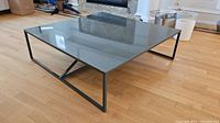Full view of the square coffee table showing glass top and black metal frame base