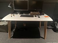Front view of white computer table with wooden legs, shows full table size and top surface