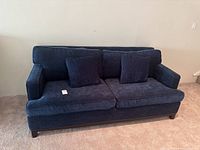 Full view of navy blue upholstered couch with two seat cushions and two throw pillows on carpeted floor