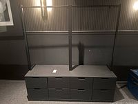 Full view of black dresser with attached metal clothes hanging rack showing 8 drawers and hanging space on top.