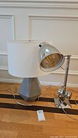 Both lamps on the floor showing the metal swivel arm lamp and ceramic lamp with white shade