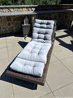 Patio lounger shown fully reclined with gray tufted cushion in sunny outdoor setting, detail of cushion and wicker frame.