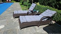 Two loungers and side table arranged poolside on stone patio.