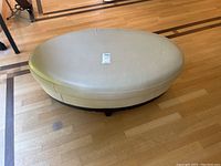 Top view of the oval cream ottoman showing surface scratches and an attached label in the center.