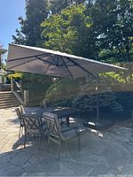 Full view of gray cantilever umbrella shading patio table and chairs on stone patio