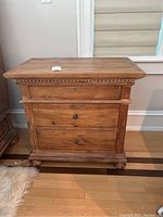 Front view of one side table showing three drawers, bun feet and molded trim