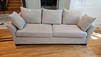 Front view of the sofa showing three back cushions and two side cushions in light gray fabric upholstery, placed on hardwood floor.