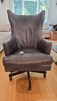 Front view of a green pleather office swivel chair showing wear and high backrest with wing-like sides and padded armrests.
