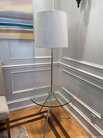 Full view of the glass table with metal legs and built-in lamp with white fabric shade