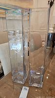 Front view of two tall clear glass vases side by side on table showing their height and square base.