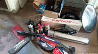 Full lot of automotive items including booster cables, battery charger, traction aid, and WD-40 cans on the floor.