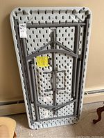 View of table folded with underside visible showing metal folding legs and plastic top underside reinforcement pattern.