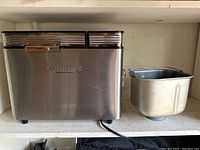 Front view of bread maker and removable bread pan showing stainless steel finish and power cord.