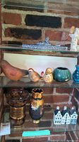 Shelf displaying various decorative items including ceramic birds, nesting doll, blue-green glass vase, textured stone figure, and ceramic houses.