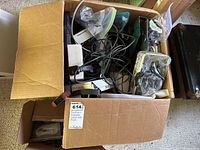 Top view of an open cardboard box filled with assorted cables, chargers, and small electronic devices mostly black and white color.