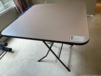 Side view of portable folding table showing brown tabletop and black folding metal legs