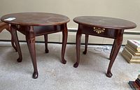 Pair of matching wooden side tables shown from one angle, featuring curved legs and round tops.