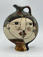 Front side of the round, flat vase showing stylized cubism face artwork with two profiles merged into one image in black and brown on beige ceramic base.