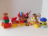 Front angled view of 14 assorted toy figures including Little People blocks, Ironman figurine, Minion toy, horse on wheels, archer, and small animal figures