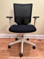 Front view of black and white office chair with black mesh back and black fabric seat on white base with wheels on hardwood floor.