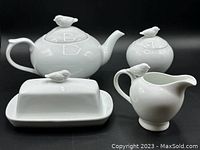 Photo of full set showing teapot, sugar bowl, creamer, and butter dish all decorated with small bird figurines on top.