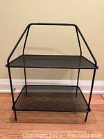 Front view of black metal mesh 2-tier stand with handle, showing overall structure and design.