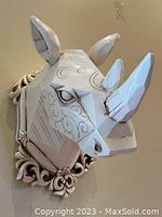 Front and side view of large geometric rhino head wall decor mounted on wall, showing horns, ears, and swirling carved details.