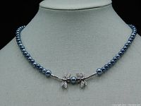 Full necklace on display stand showing dark gray and black pearls with central silver-colored dragonfly pendant.