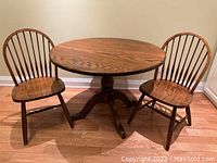 Full view of the round oak table with two Windsor-style chairs placed on either side, showing the overall size and style.