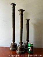 Set of three tall brass column candlesticks of different heights with a 7up can for scale