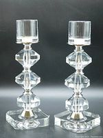Pair of clear Slovenian crystal pedestal candle sticks with heavy rectangular bases, octagonal crystal pieces separated by silver linear spacers, and round glass candle holders on top.