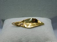 Single 10 karat gold leaf pendant displayed on a white fabric surface to show shape and finish.